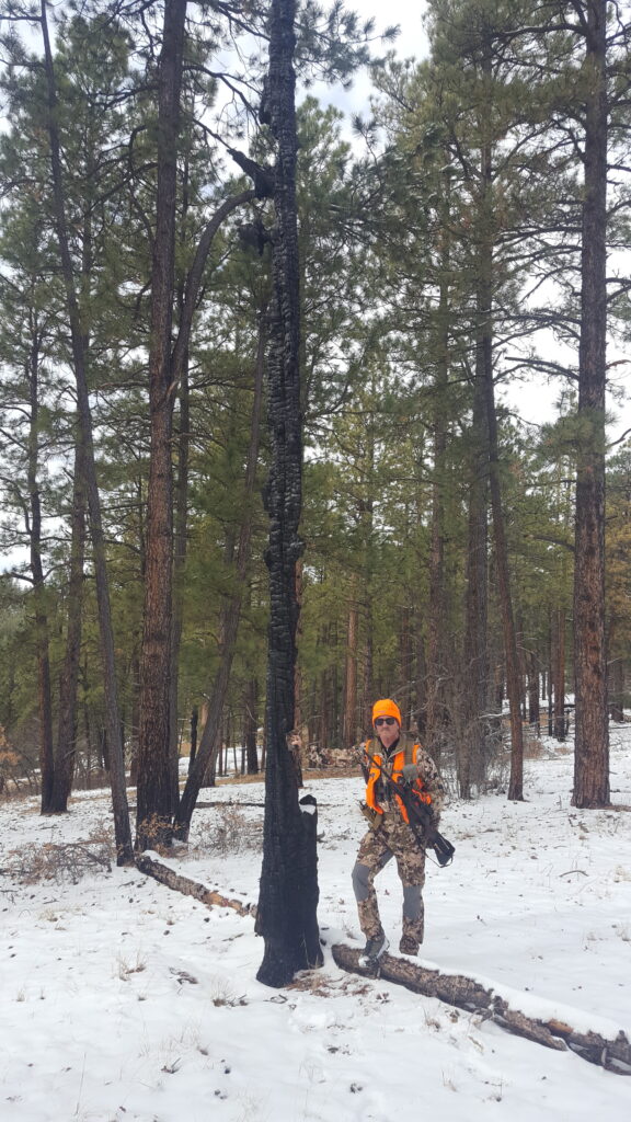 DIY hunting gear setup tips - Gerald Gerwick and his hunting gear setup standing in the snow and leaning on a pine tree