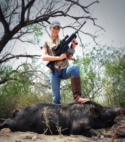 Lady hunting standing over a large wild hog she shot using her rifle