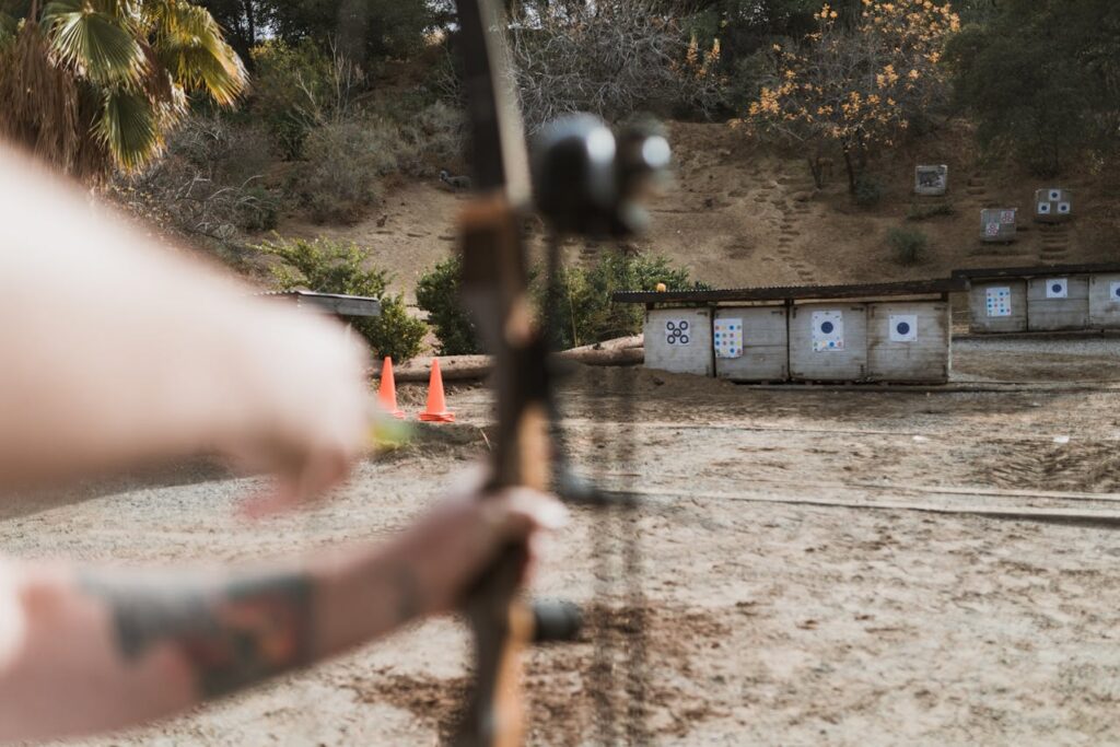 Over-the-shoulder photo of an archer drawing is bow with the target in the background.