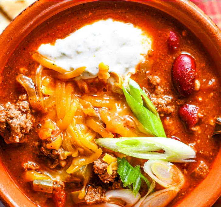 Bowl of venison chili topped with cheese and sliced green onions.