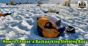 What to Look for in a Backpacking Sleeping Bag featured image showing a lady backpacker in her sleeping bag in the middle of a snow field.